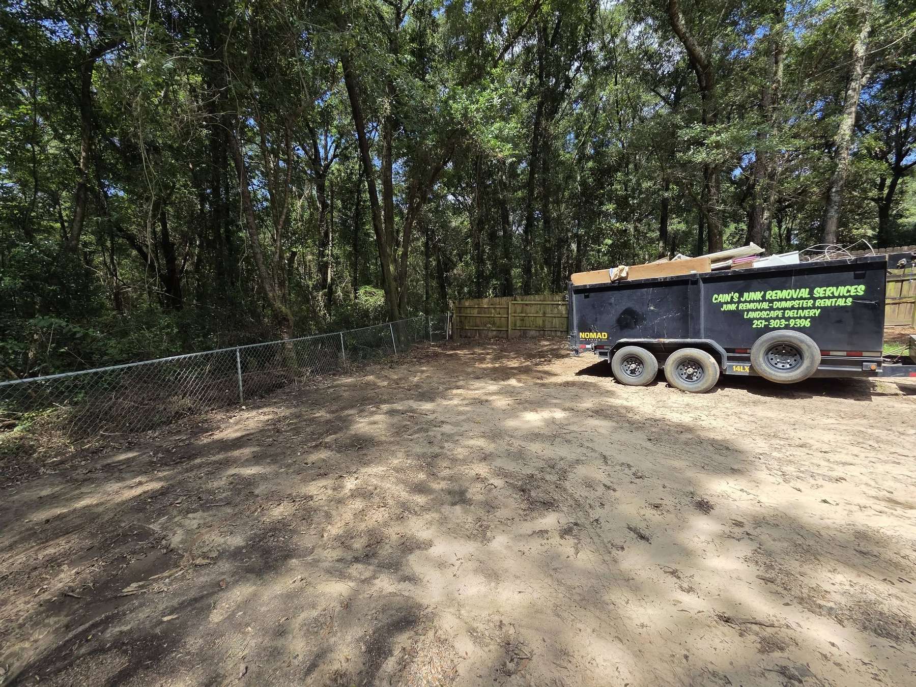 Cain's black 14-yard dump trailer loaded with debris, parked in a freshly cleared yard.
