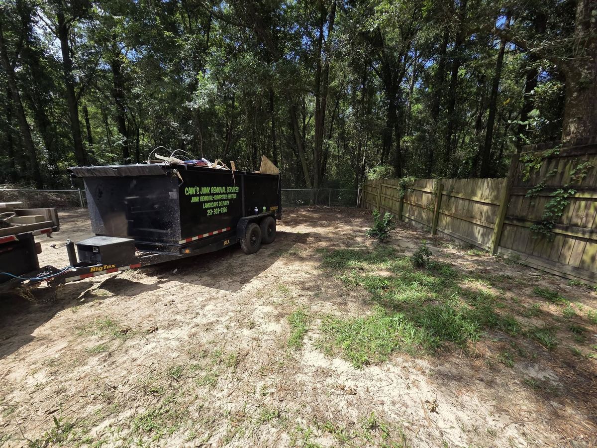 Cain's black 14-yard dump trailer parked in a cleared backyard, loaded with debris.